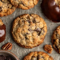 A chocolate chip cookies with chocolate chips, chocolate chunks, pecans and oatmeal on parchment paper for an upclose look at the texture.