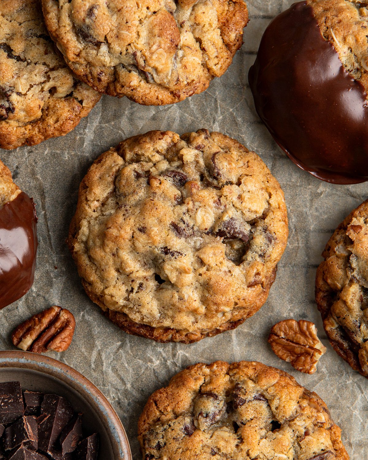 A chocolate chip cookies with chocolate chips, chocolate chunks, pecans and oatmeal on parchment paper for an upclose look at the texture.