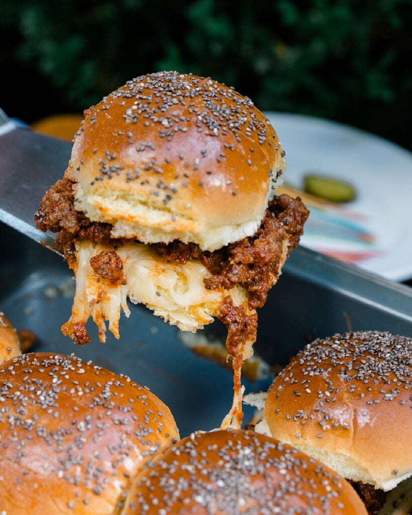 Pulling a sloppy joes slider from the pan they baked in with a cheese pull keeping the bun from getting soggy.