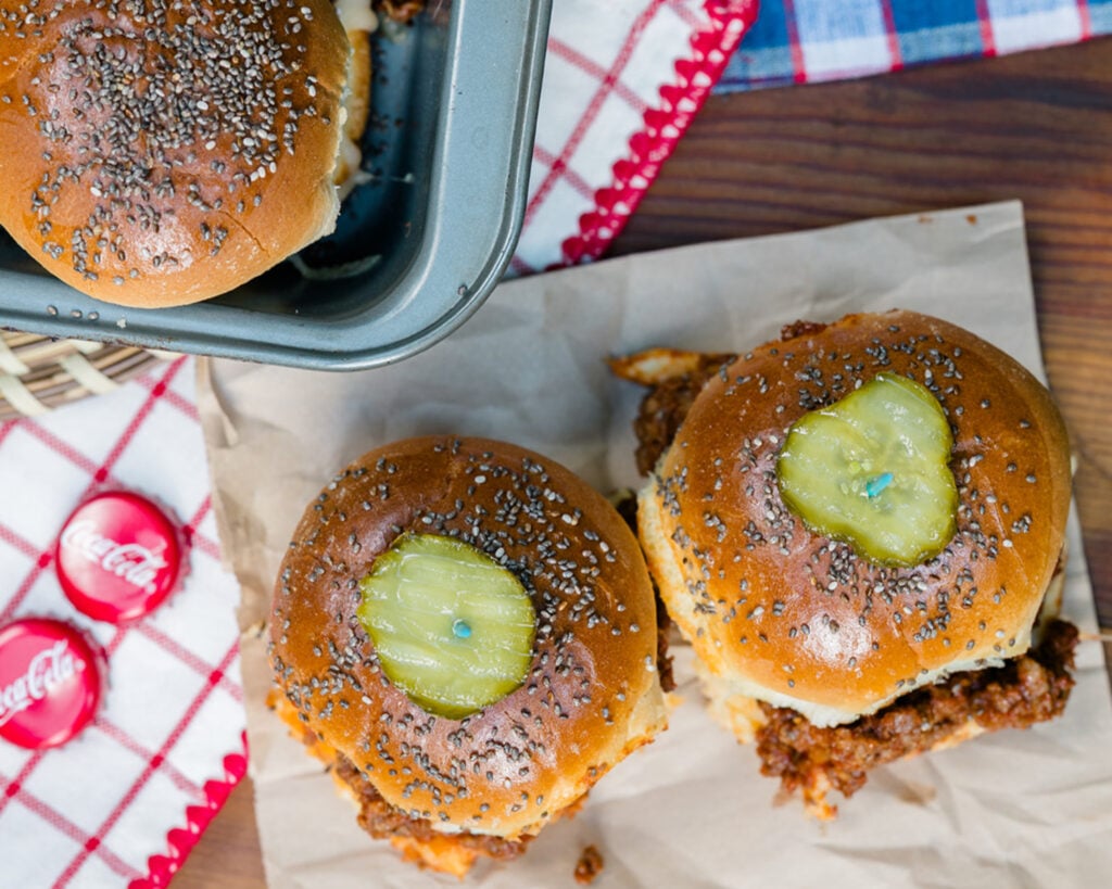 Looking down on 2 sloppy joes sliders with homemade sauce, topped with chia seed buns and a pickle as a serving suggestion for those making the recipe.