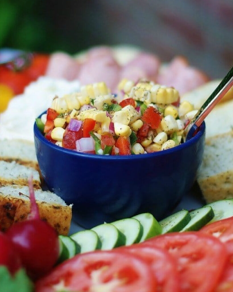 Marinated corn salad in a blue bowl on a crudite platter.