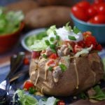 A baked potato stuffed with spicy sausage queso, lettuce, tomatoes and sour cream.