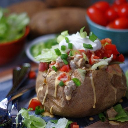 A baked potato stuffed with spicy sausage queso, lettuce, tomatoes and sour cream.