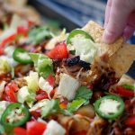 Someone pulling a nacho from a sheet pan BBQ Nacho.