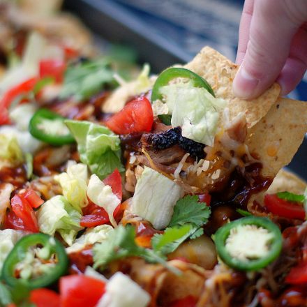 Someone pulling a nacho from a sheet pan BBQ Nacho.