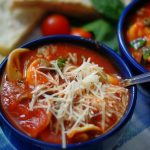 An upclose of a bowl of tortellini soup with parmesan cheese on top.