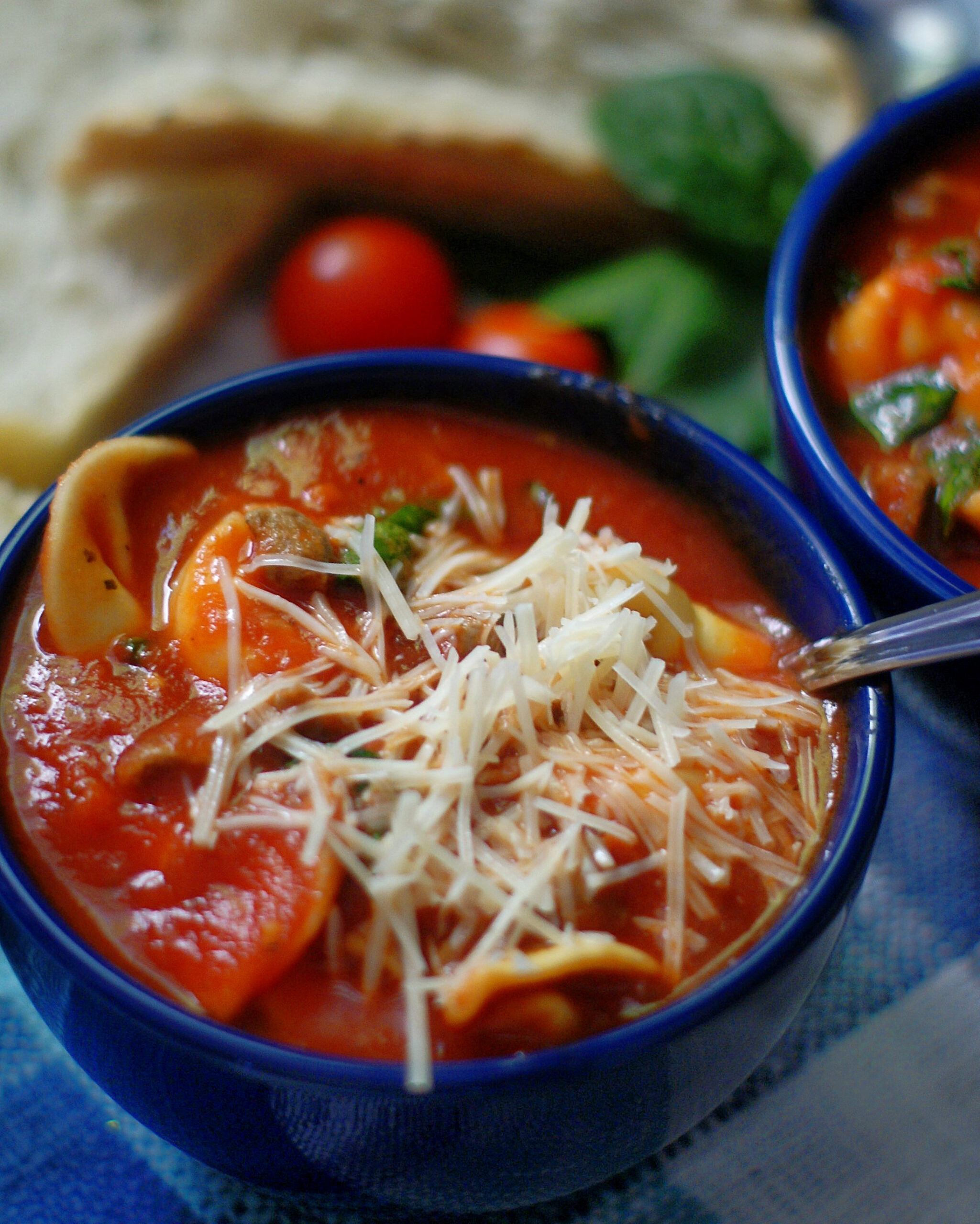 An upclose of a bowl of tortellini soup with parmesan cheese on top.