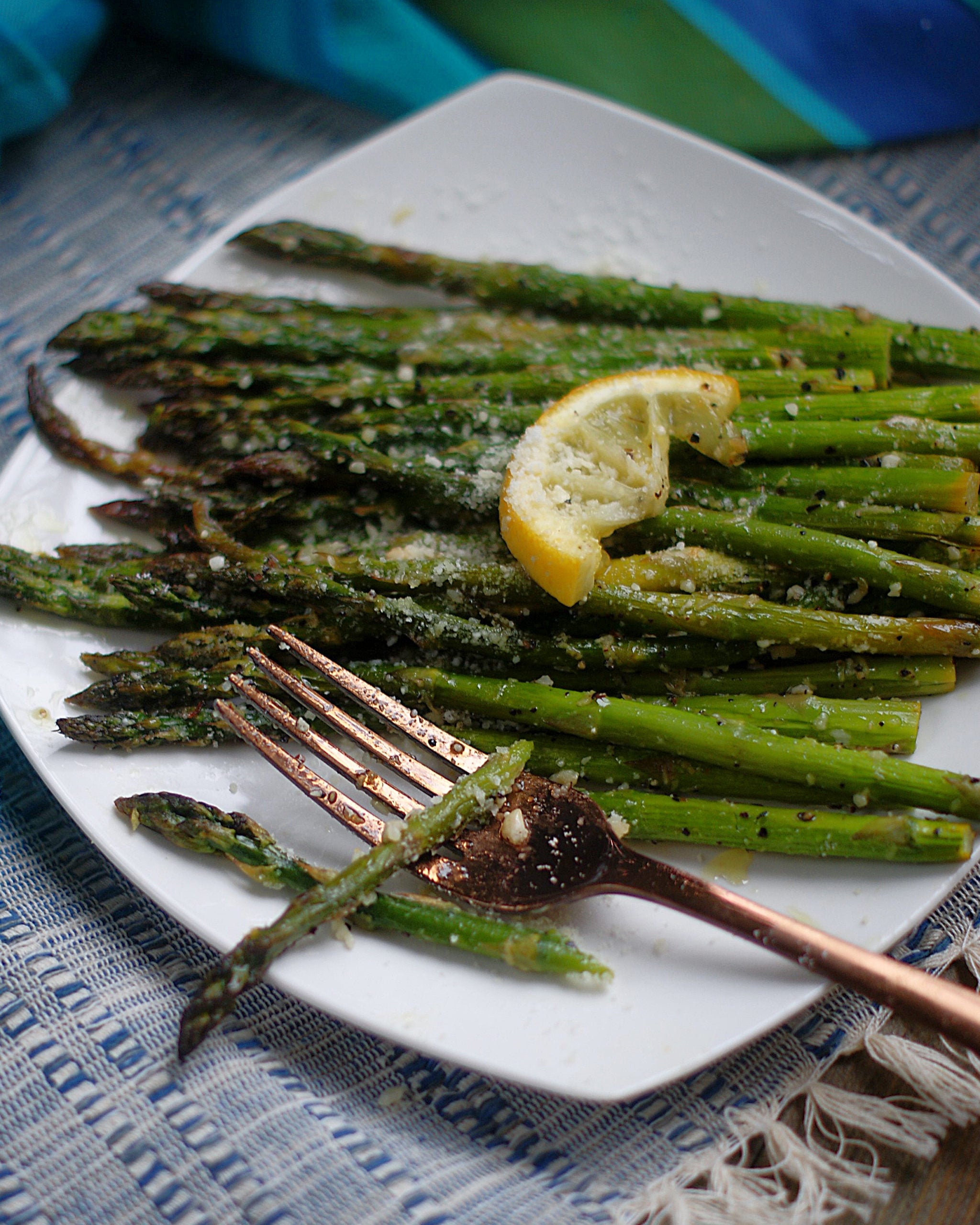Roasted Lemon Asparagus on a white plate with a slice of lemon and parmesan cheese.