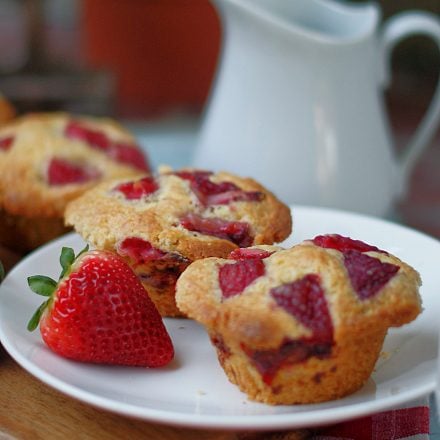 2 large farm style strawberry buttermilk muffins on a white plate with a white milk pitcher in the background.