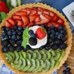 A completed fruit tart garnished with whipped topping and more fruit.