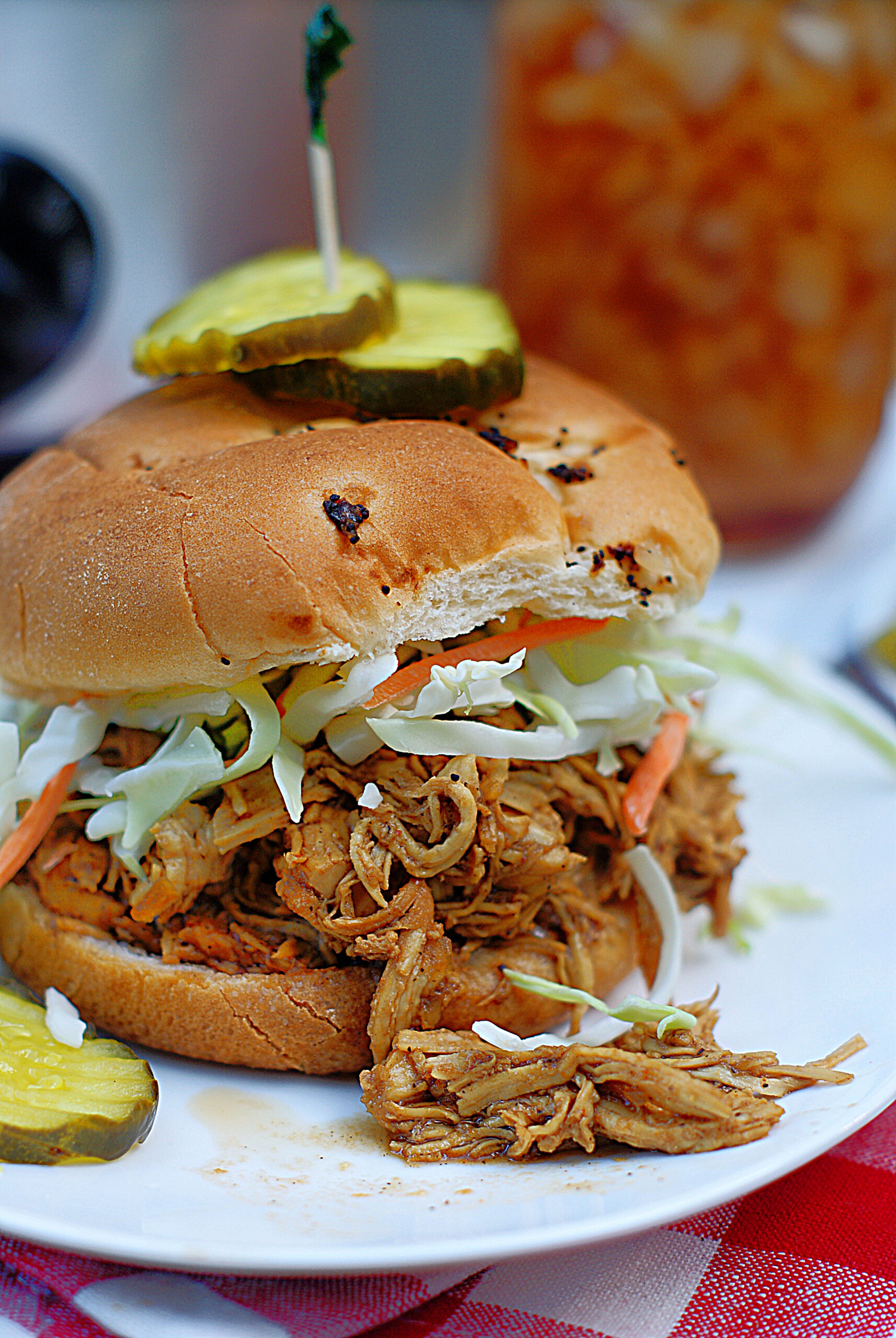 An up close of a shredded BBQ chicken sandwich with pickles and coleslaw.