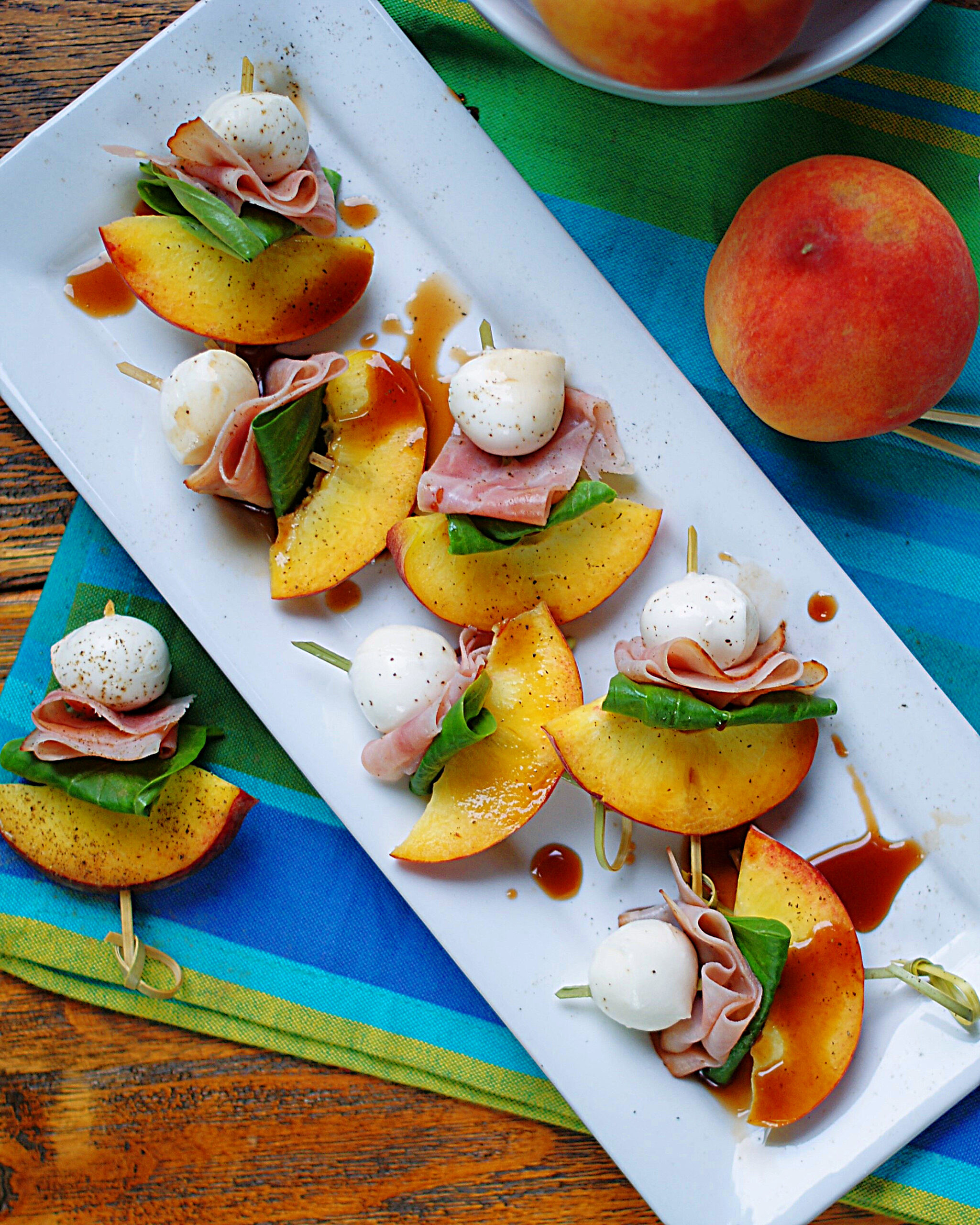 A party tray of peach skewer with mozarella, ham, basil and balsamic appetizers.