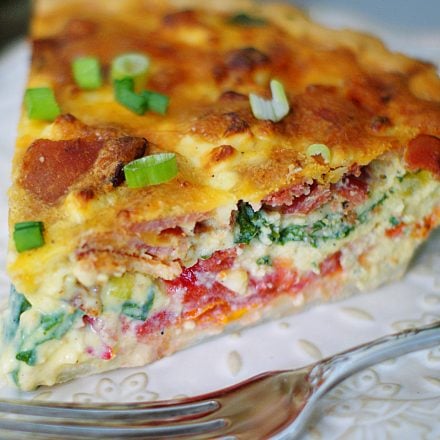 An upclose of a BLT Quiche slice, filled with tomatoes, bacon, spinach, green onions and cheese.