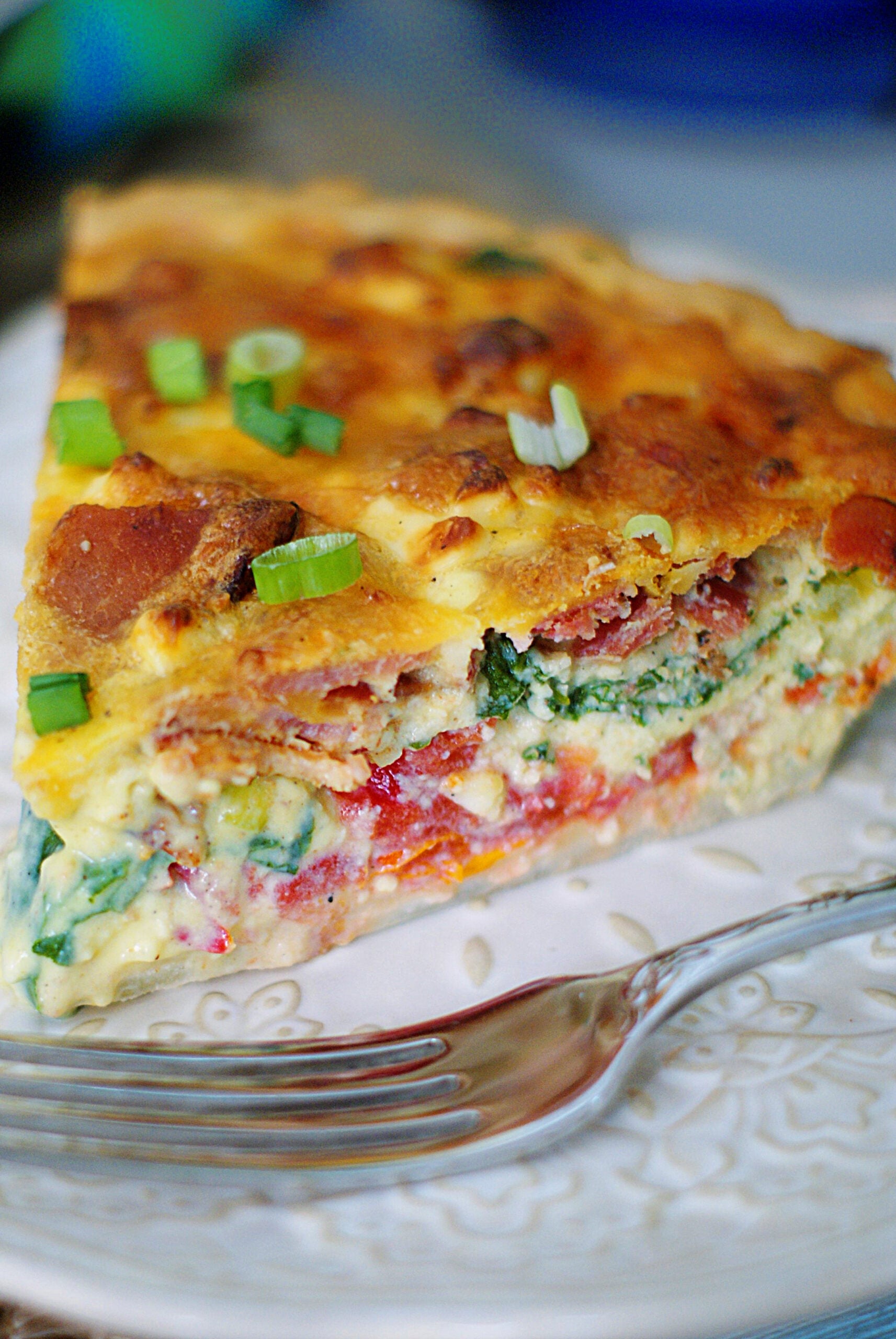 An upclose of a BLT Quiche slice, filled with tomatoes, bacon, spinach, green onions and cheese.