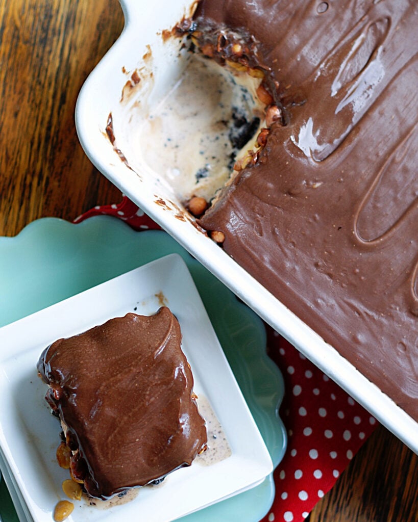 Looking down on a 9x13 Buster Bar dessert with a slice served on a plate to show the glossy chocolate topping, how the dessert looks in the 9x13 and how it can be served.