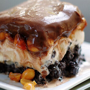 A slice of Buster Bar Dessert showing the distinct layers of ice cream, oreo cookie crust, peanuts and homemade chocolate topping.