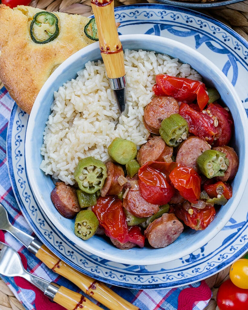 A close up of fresh stewed tomatoes and okra served with rice to show the texture of the vegetables and smoked sausage.