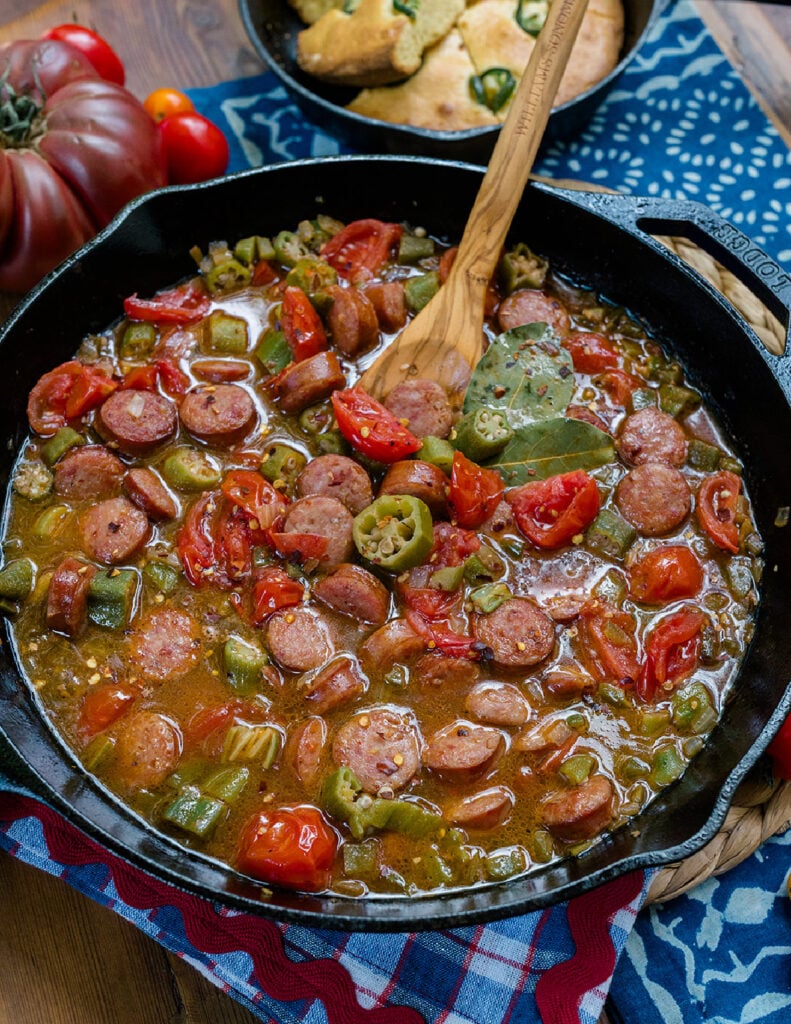 Smoked Sausage smothered in stewed tomatoes and okra in a cast iron skillet with cornbread on the side.