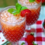 Two glasses of strawberry tea garnished with strawberries and mint.