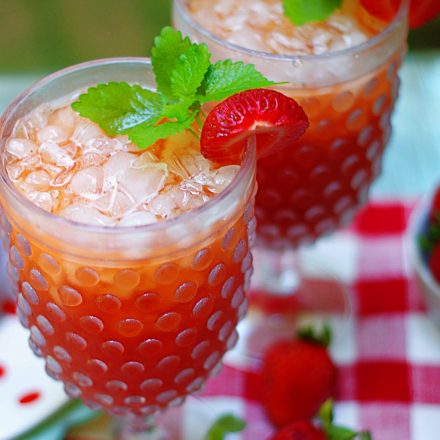 Two glasses of strawberry tea garnished with strawberries and mint.