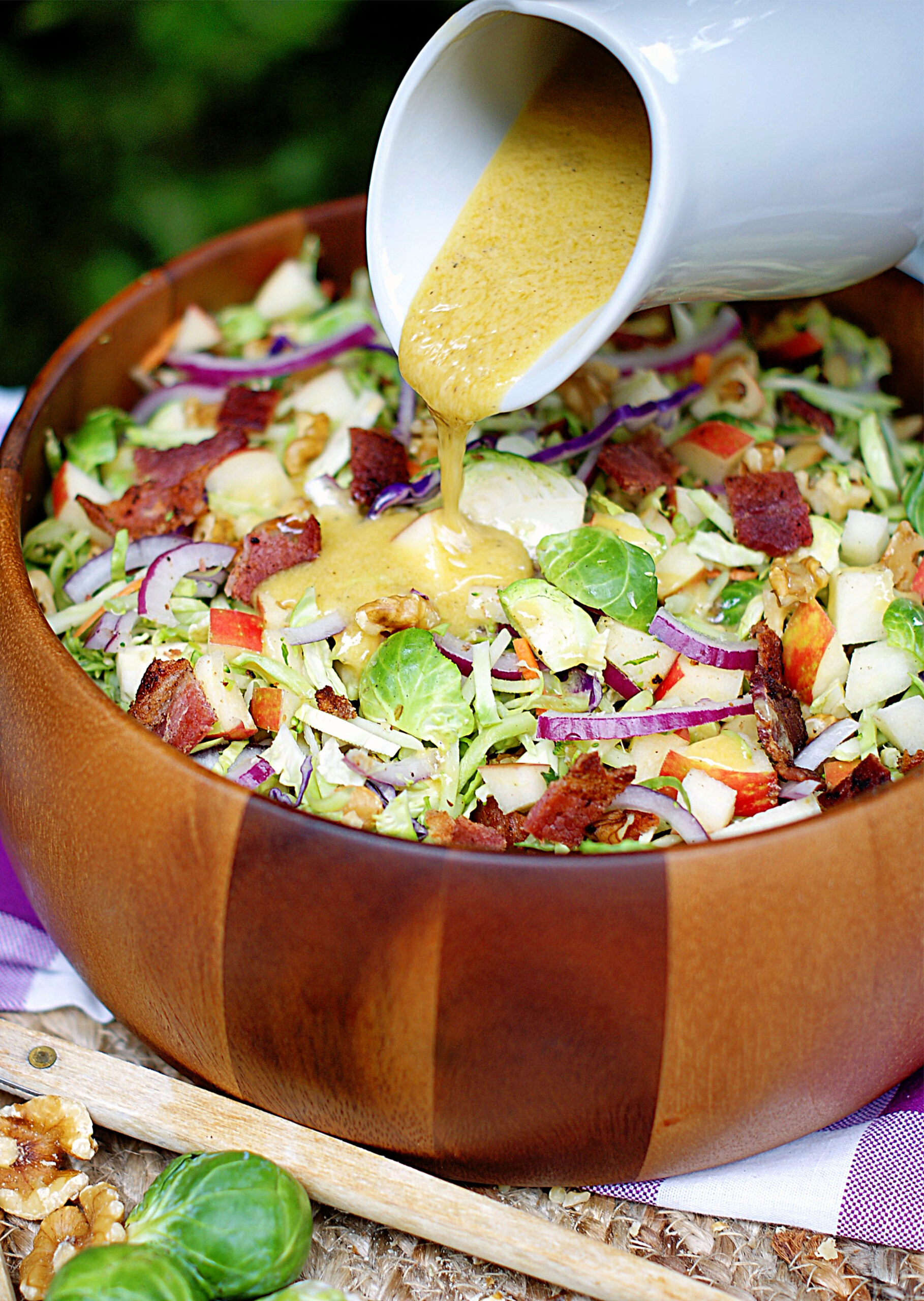 Dijon Dressing being poured over the broccoli slaw with apples and brussel sprouts