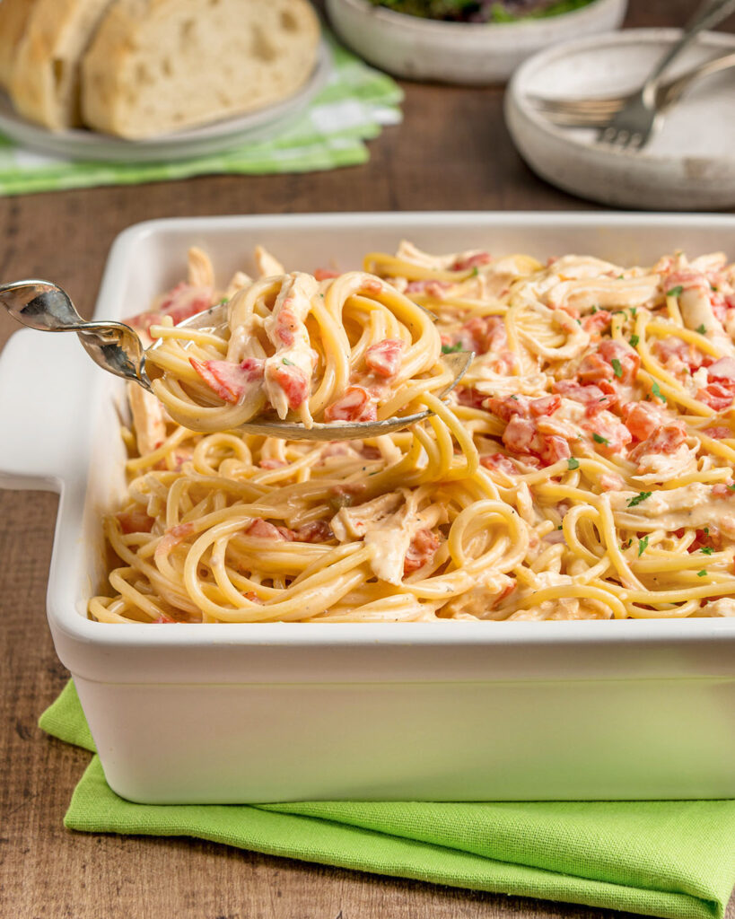 A serving spoon full of Rotel chicken spaghetti and a baking dish showing how this pasta casserole would be served at dinner for a family.
