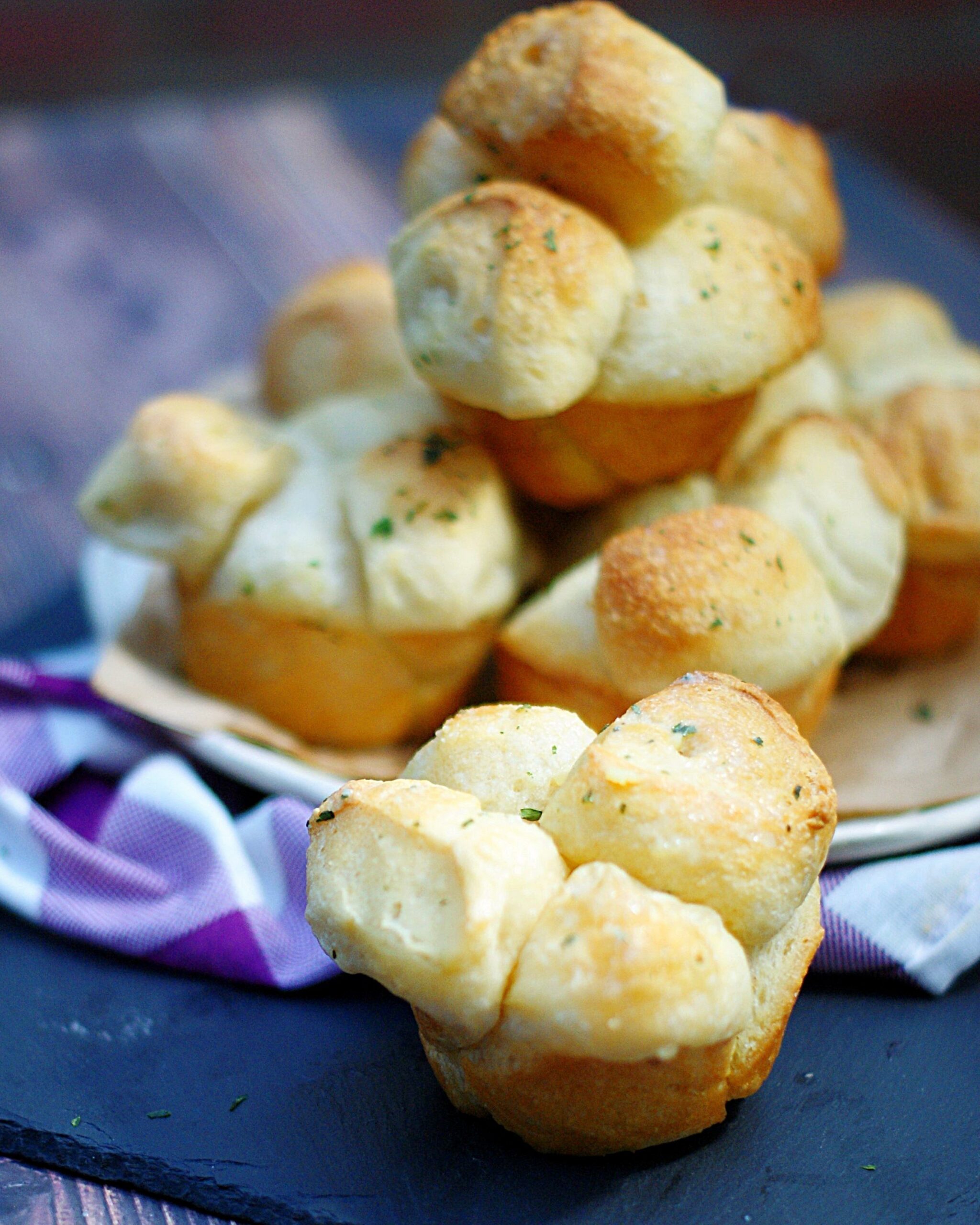 A close up of a shortcut pull apart roll with a plate full of buttery rolls behind it.