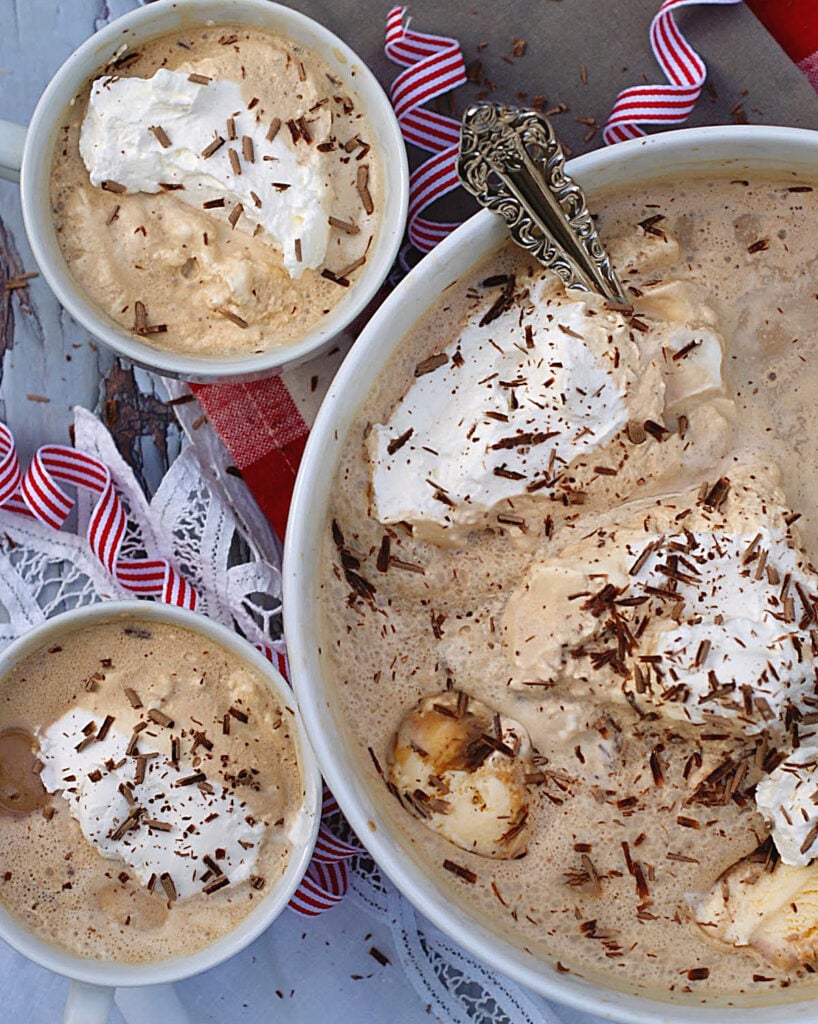 Coffee Punch in a white punch bowl topped with chocolate shavings and dollops of whipped cream. with 2 cups to the side.