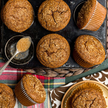Homemade gingerbread muffins in a muffin tin with a spoonful of turbinado finishing sugar.