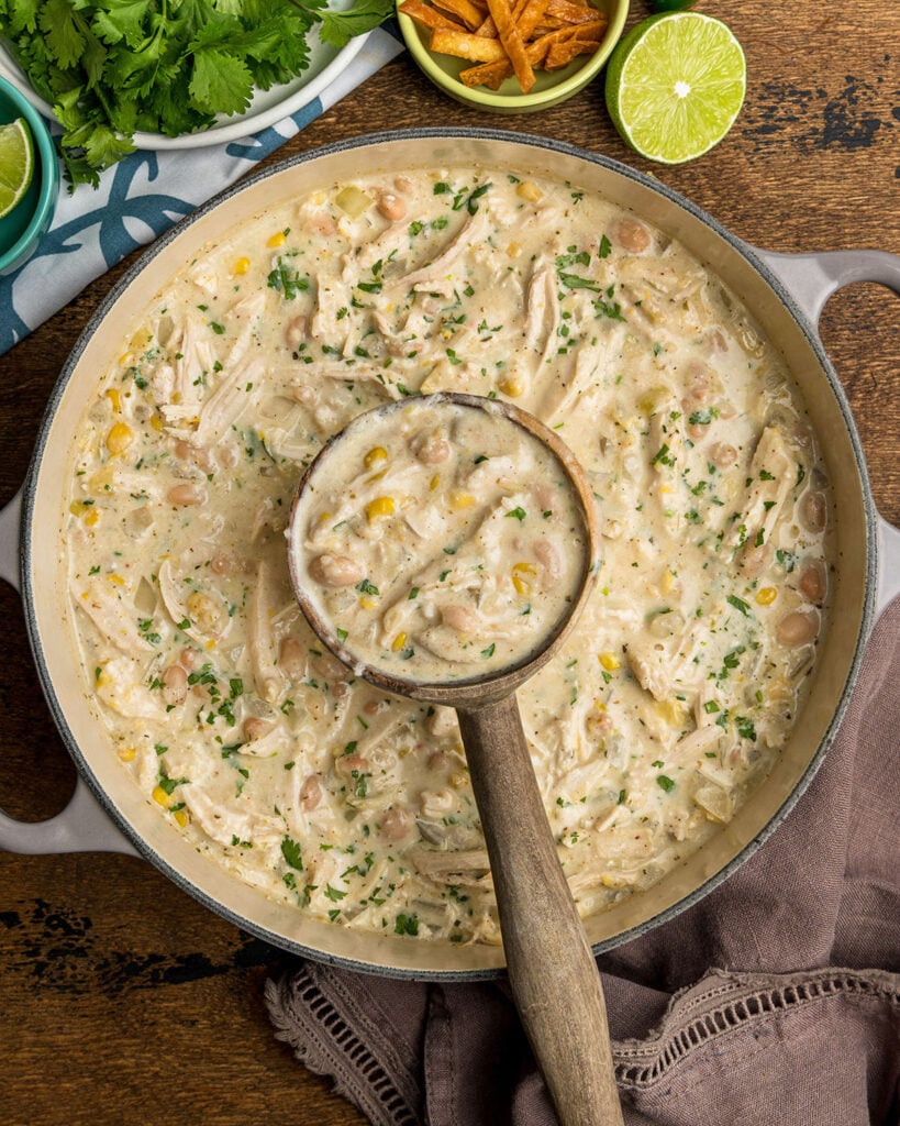 A pot of white chicken chili with a wooden ladle spooning up a serving of chili to show texture and hearty ingredients.