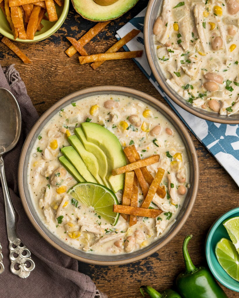 A bowl of cream cheese chicken chili topped with tortilla strips, avocados to show how it can be served.