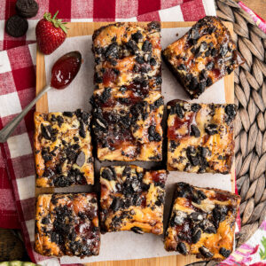 A batch of strawberry jam brownies on parchment paper with a spoon of jam.