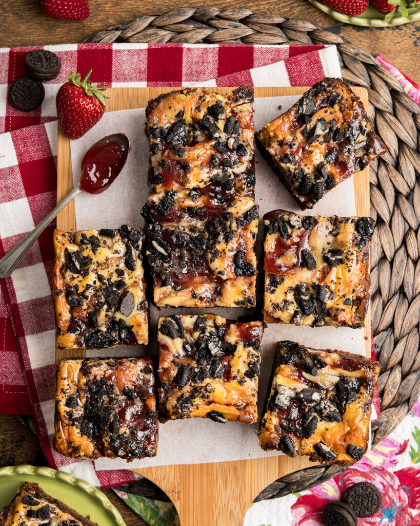 A batch of strawberry jam brownies on parchment paper with a spoon of jam.