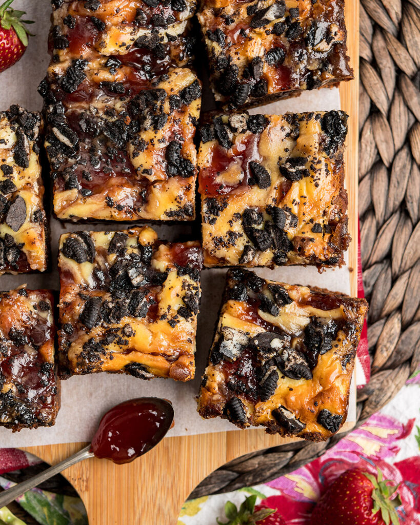 Looking down on freshly sliced brownies to show the texture of the strawberry jam, cheesecake layer and cookies on top of the brownies.