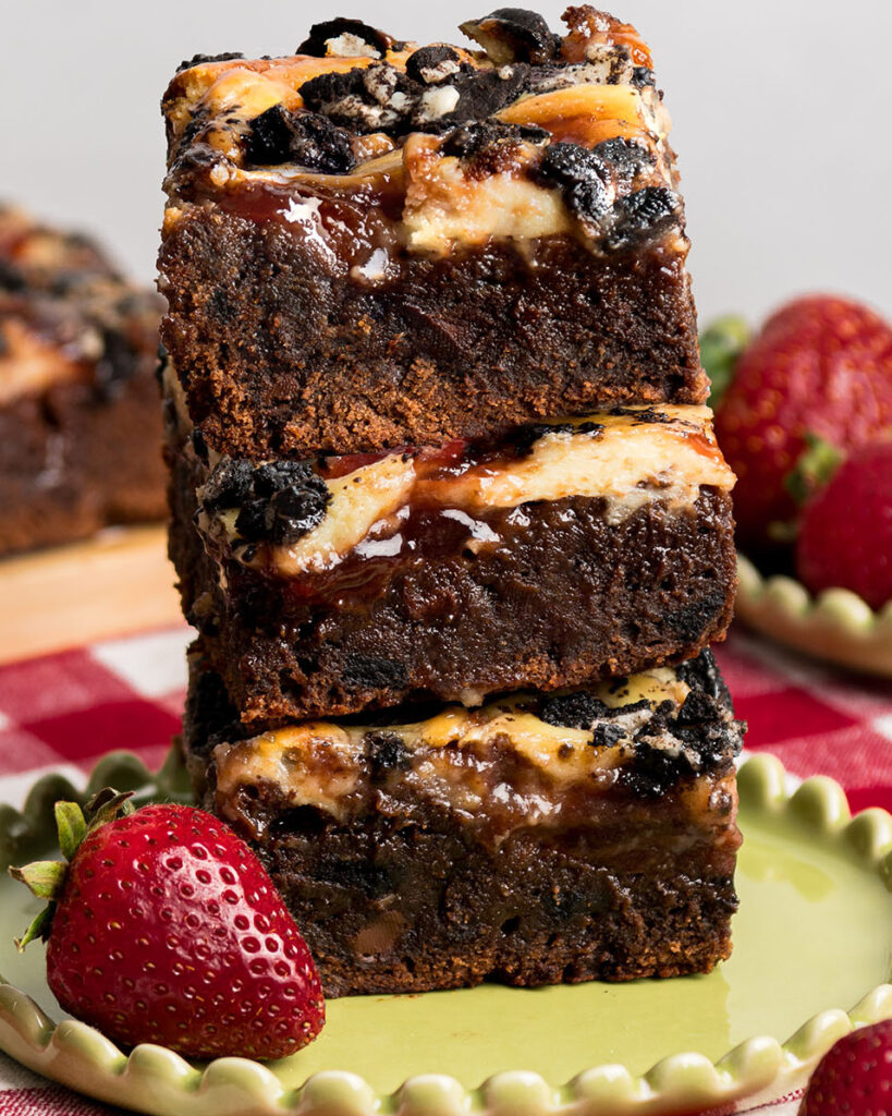 3 homemade brownies with strawberry jam stacked on top of each other to show the thickness of the brownies.