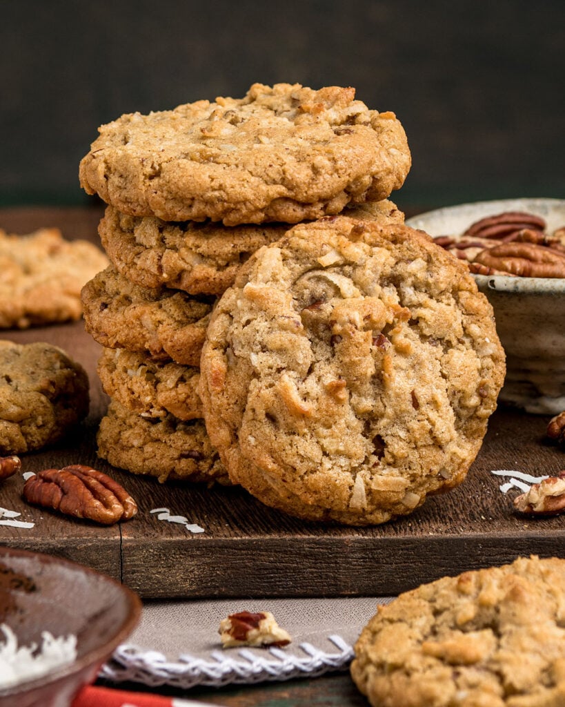 A stack of 5 chewy coconut pecan cookies and 1 extra cookie propped against the stack to show golden color and texture.