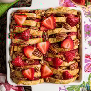 Looking down on Strawberry French Toast Casserole with slices of French bread, strawberries and halved pecans in a white casserole dish.