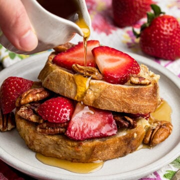 Two slices of strawberry French Toast with brown sugar pecan topping with maple syrup being drizzled over the top.