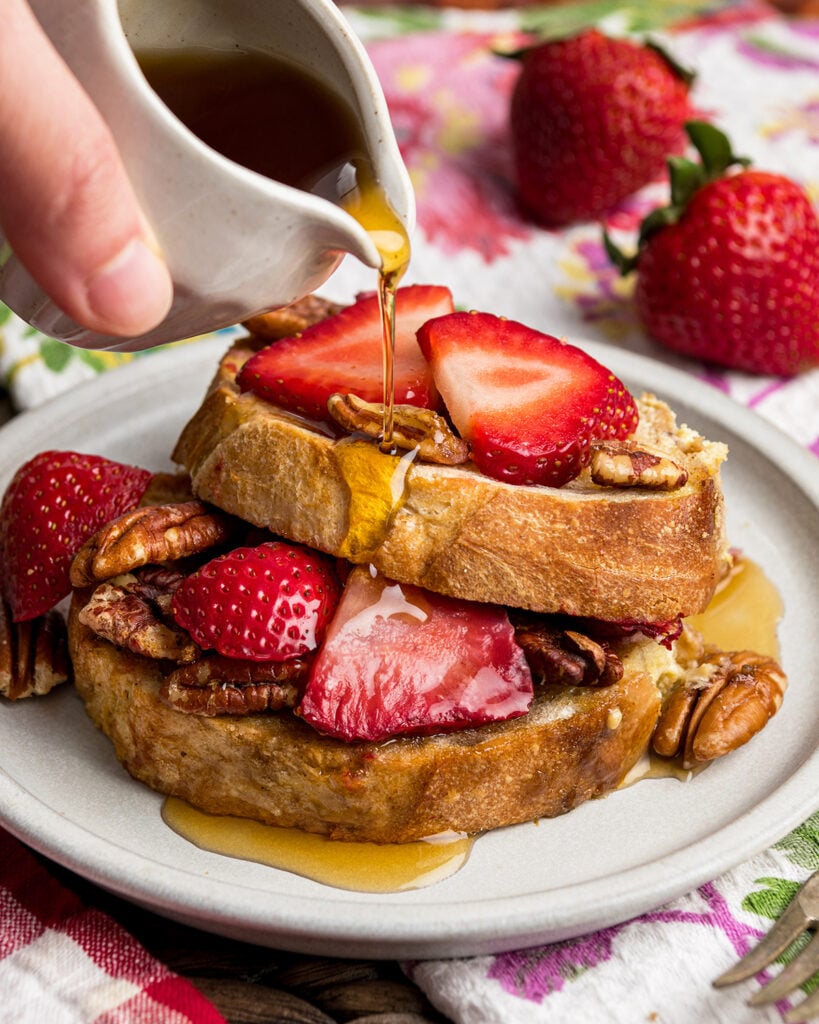 Two slices of strawberry French Toast with brown sugar pecan topping  with maple syrup being drizzled over the top.