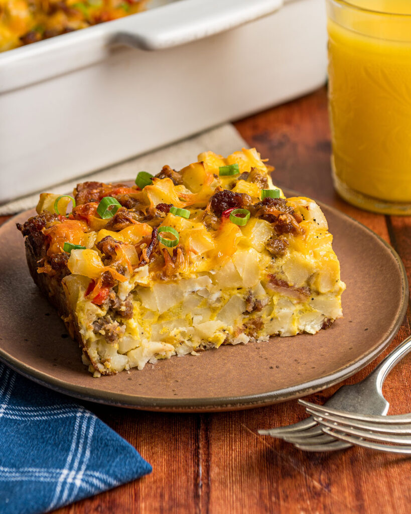 A slice of hash brown casserole with eggs and sausage and bacon shown from the side to show the ingredients and texture.