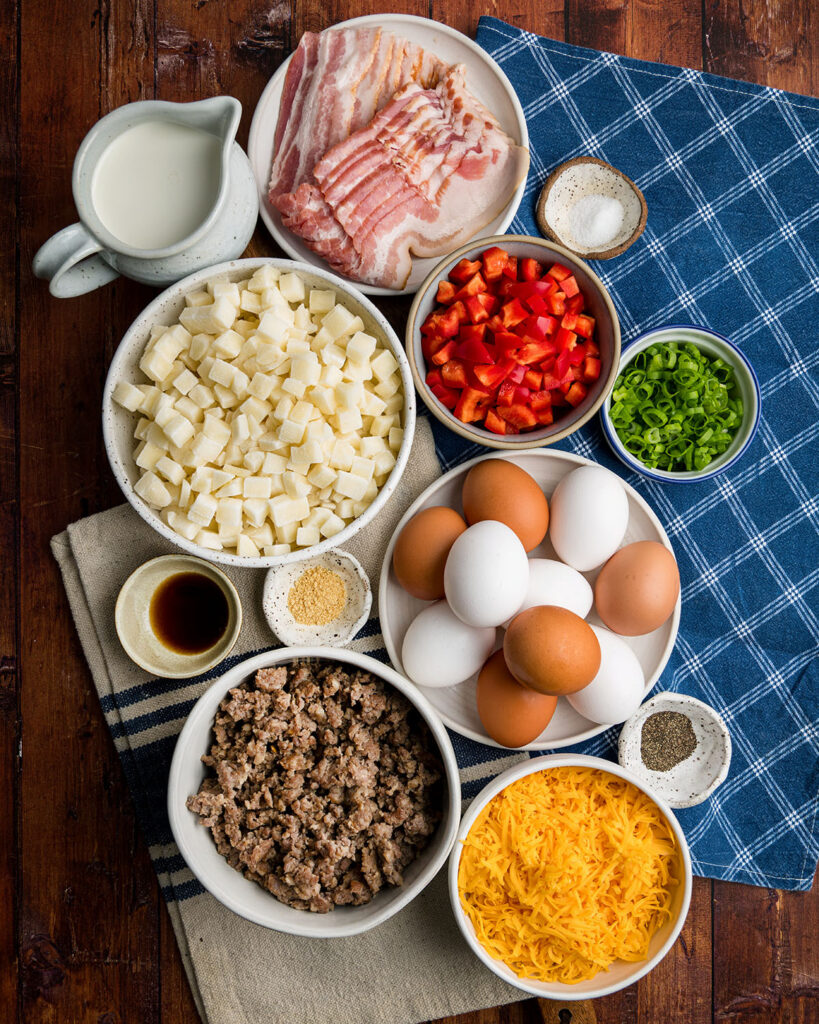 The ingredients to make a Farmer's Breakfast Hash brown casserole laid out on plates next to a blue dinner napkin as a visual ingredients list to support the written one.