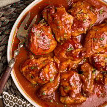 A serving platter filled with southern BBQ chicken thighs, accompanied by a meat fork and topped with chopped parsley, showing how it will be served at the table.