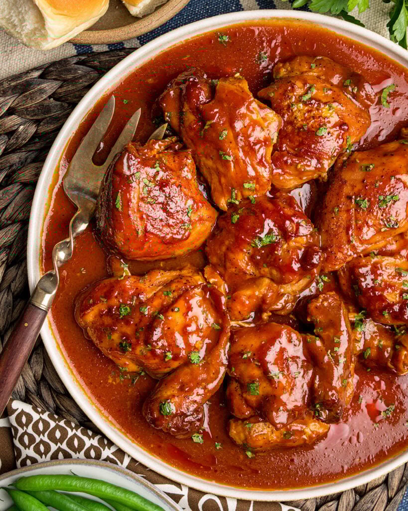 A serving platter filled with southern BBQ chicken, accompanied by a meat fork and topped with chopped parsley, showing how it will be served at the table.