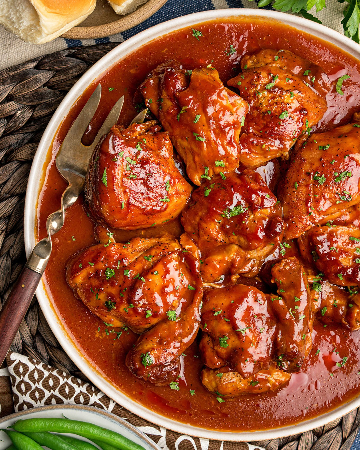 A serving platter filled with southern BBQ chicken thighs, accompanied by a meat fork and topped with chopped parsley, showing how it will be served at the table.