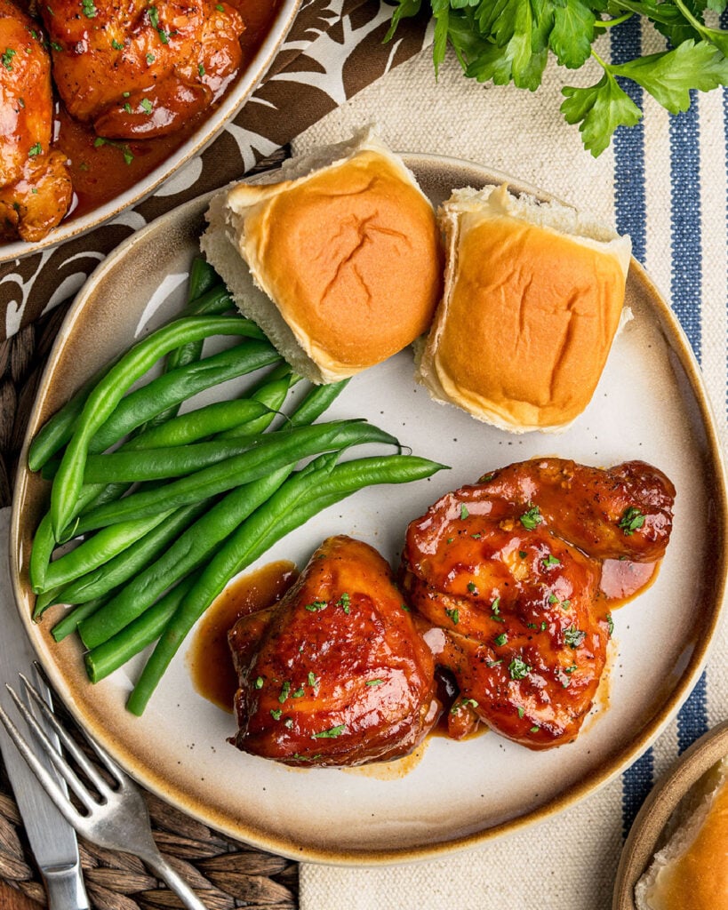 A dinner plate filled with Southern BBQ Chicken Thighs, green beans and rolls as an easy dinner idea for busy families.