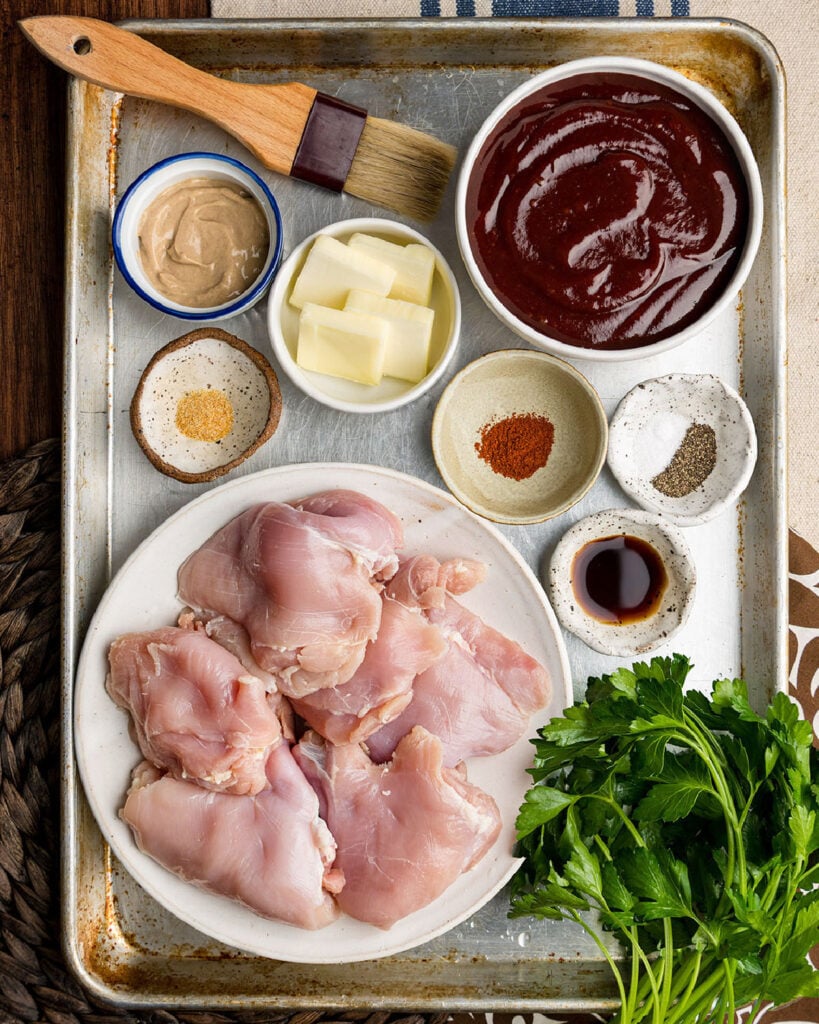 Ingredients to make crock pot BBQ chicken thighs including BBQ sauce, mustard, spices and butter.