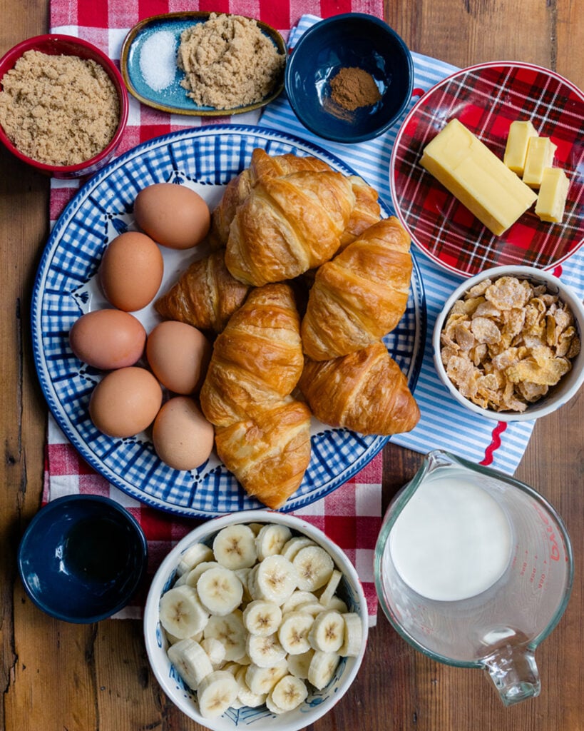 The ingredients needed to make a French Toast casserole with sliced bananas, croissants and frosted corn flakes.