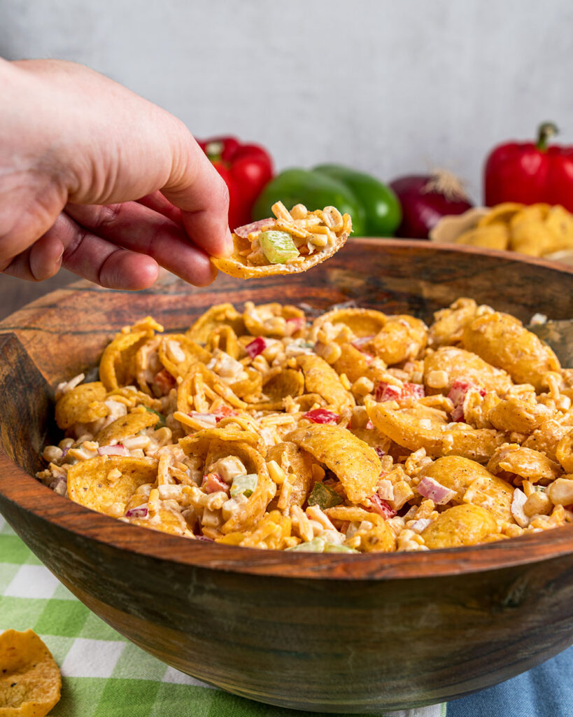 A bowl of Frito Corn Salad with someone holding a corn chip full of salad to show how it can be dipped as well as eaten with a fork.