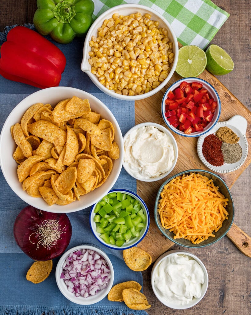 The ingredients needed for this fun corn salad, including Fritos corn chips, red and green bell pepper, purple onion and cheddar cheese.