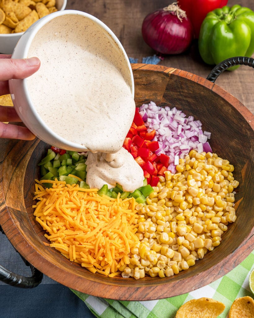 Pouring the creamy sour cream and and mayonnaise dressing seasoned with chile powder, lime and cumin over the corn and peppers before adding the chips.